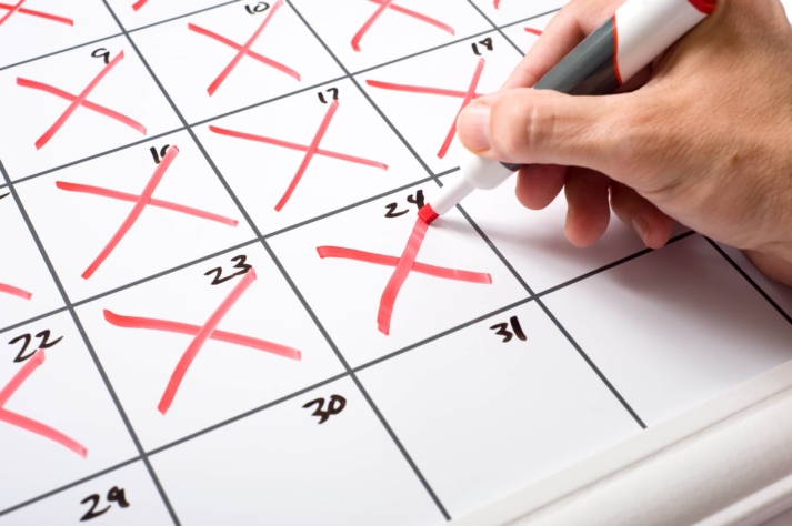 A hand making red X marks on the days of a calendar.
