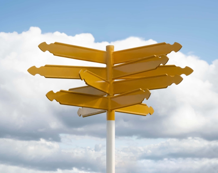 Yellow empty directional signposts against blue sky with clouds background signifying indecision or having multiple choices available.