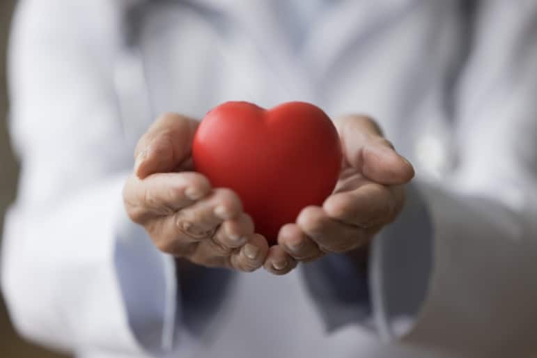 Closeup of a doctor holding a red heart symbol in their cupped hands.