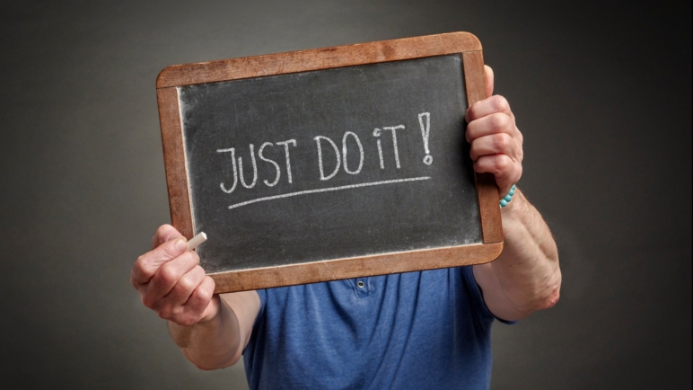 Motivational phrase, just do it, handwritten with white chalk on a blackboard held by a person in a blue shirt