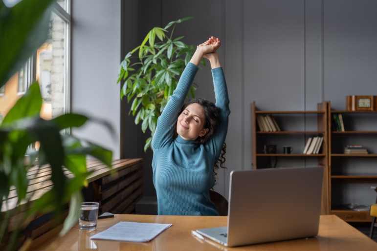 Relaxed clinician taking a stretch break between patients in a peaceful office with plants and sunlight.